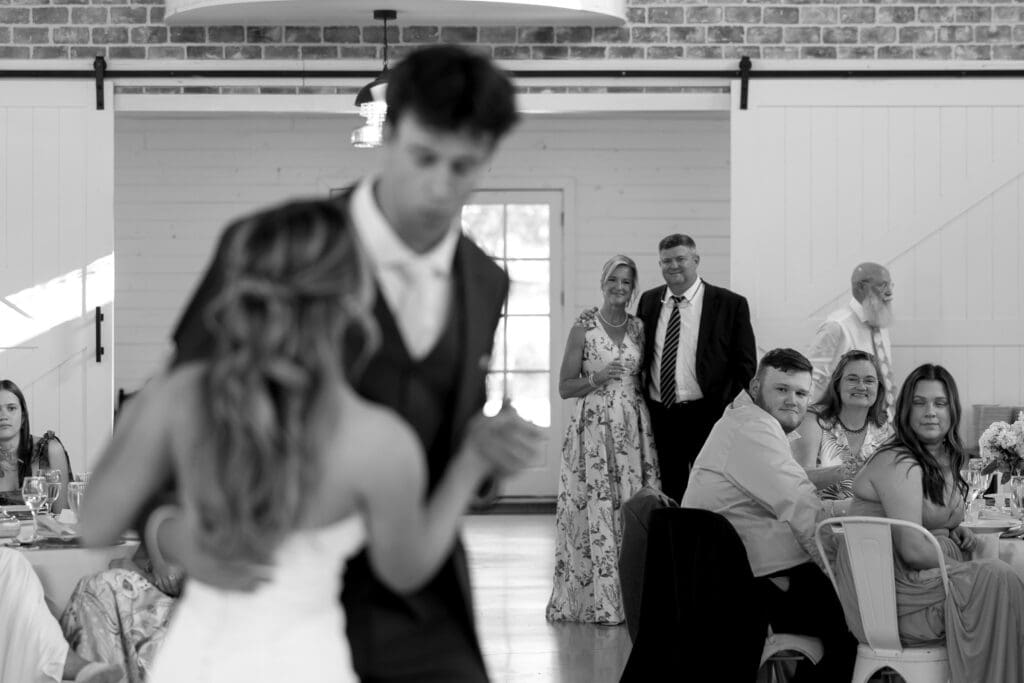 Groom’s parents watching the newlyweds share their first dance during the wedding reception