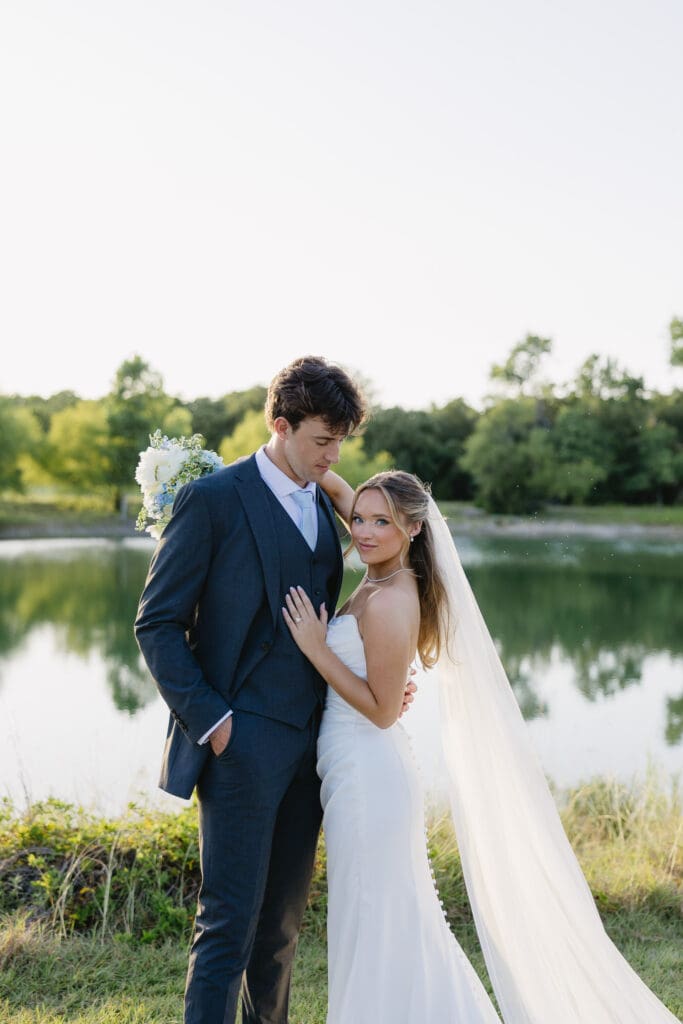 Bride and groom posing together by the pond during golden hour