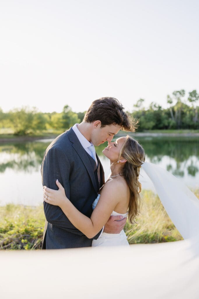 Bride and groom kissing by the water during golden hour wedding portraits